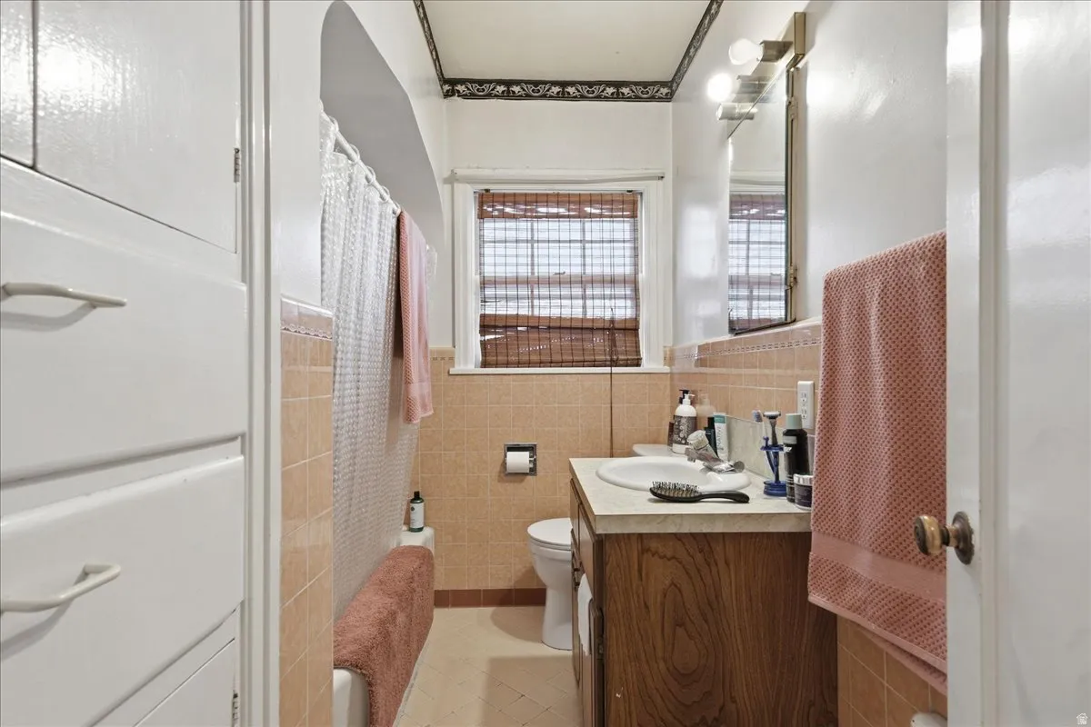 Bathroom featuring an integrated vanity with a wood-finish base and light-toned countertop, a window with natural light, tiled walls, and a built-in storage cabinet
