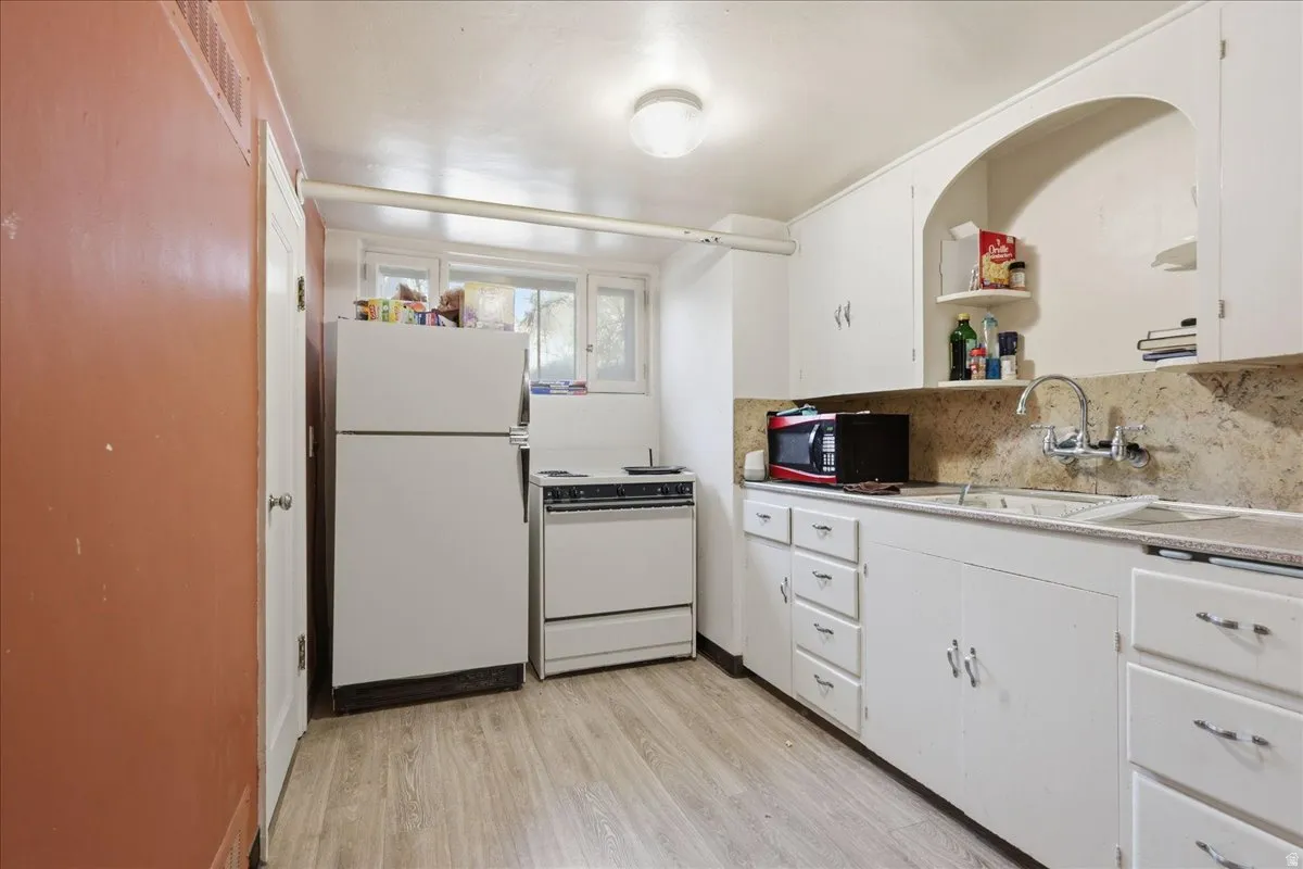 Kitchen featuring white cabinetry, wood-finish flooring, a white refrigerator, a white range, and a dual-basin sink with a chrome faucet
