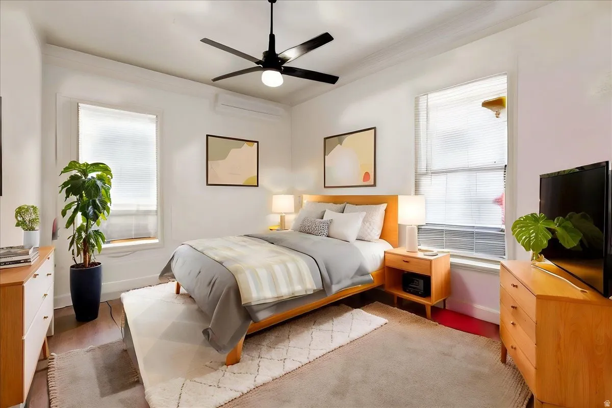 Bright bedroom featuring wood-finish flooring, two large windows, a ceiling fan, and crown molding