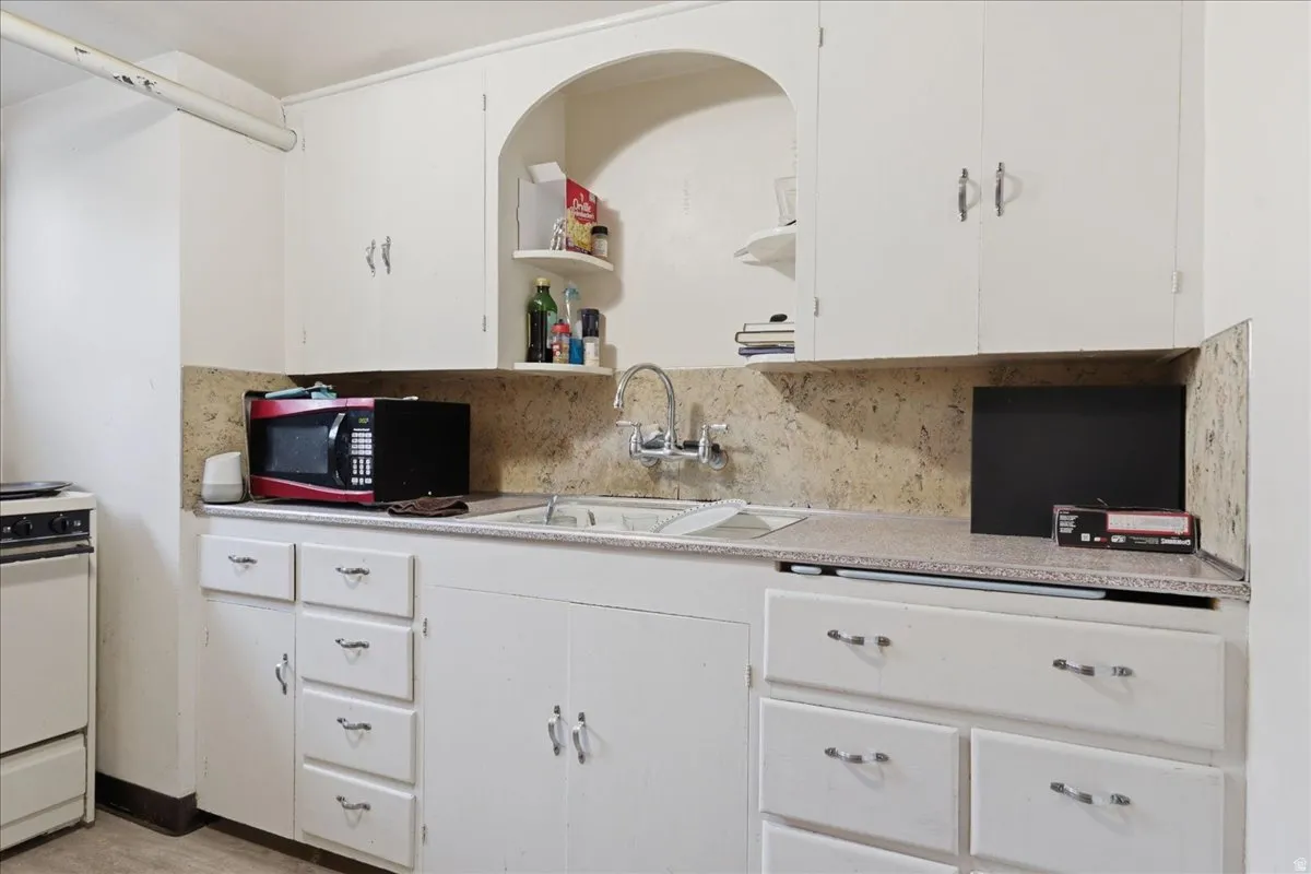 Kitchen featuring white cabinetry, light-colored countertops, a dual-basin sink with a chrome faucet, and a light-toned backsplash