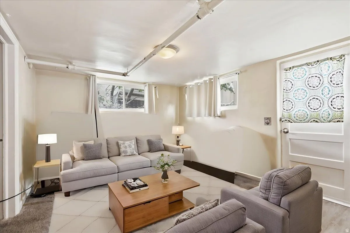 Finished lower-level space featuring recessed windows, painted ceiling beams, and a combination of carpet and wood-finish flooring