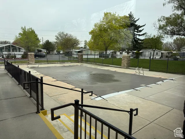 Community pool area featuring a concrete deck, black metal fencing, and stone pillars