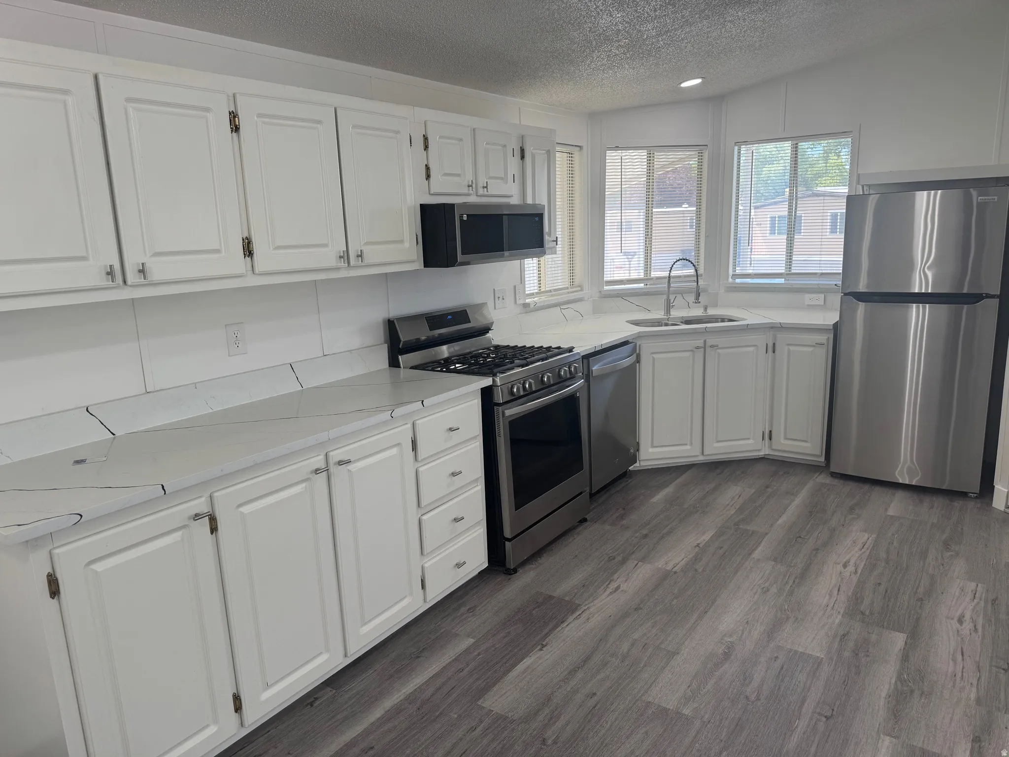 Kitchen featuring white cabinetry, light-toned countertops, stainless steel appliances, and wood-finish flooring