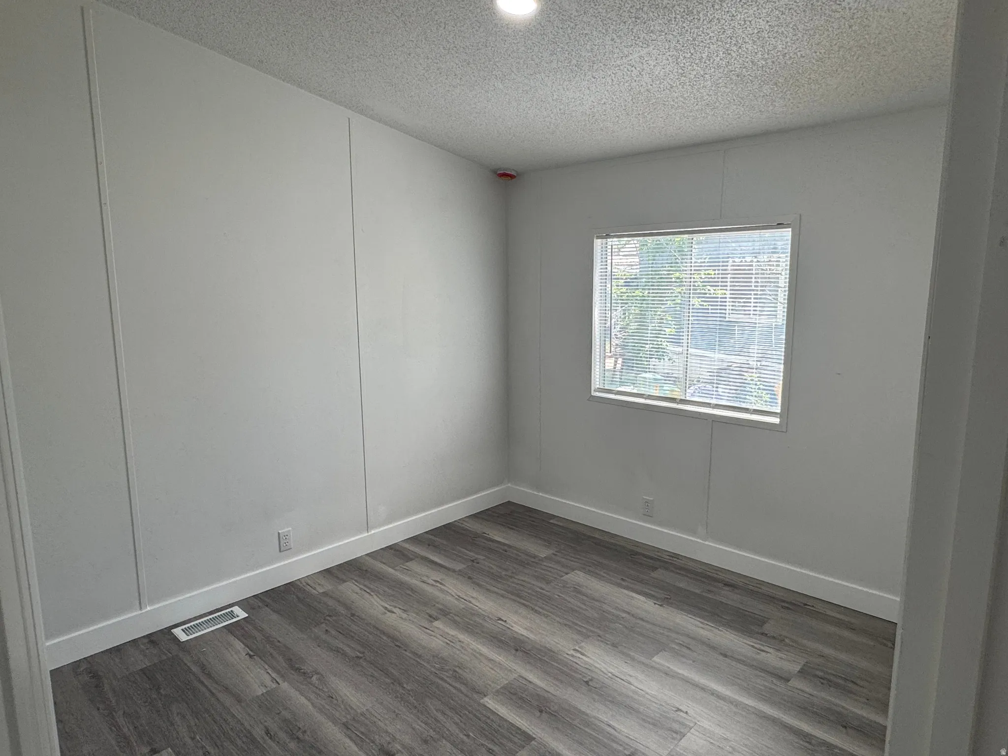 Room with wood-finish flooring, white paneled walls, and a window with blinds