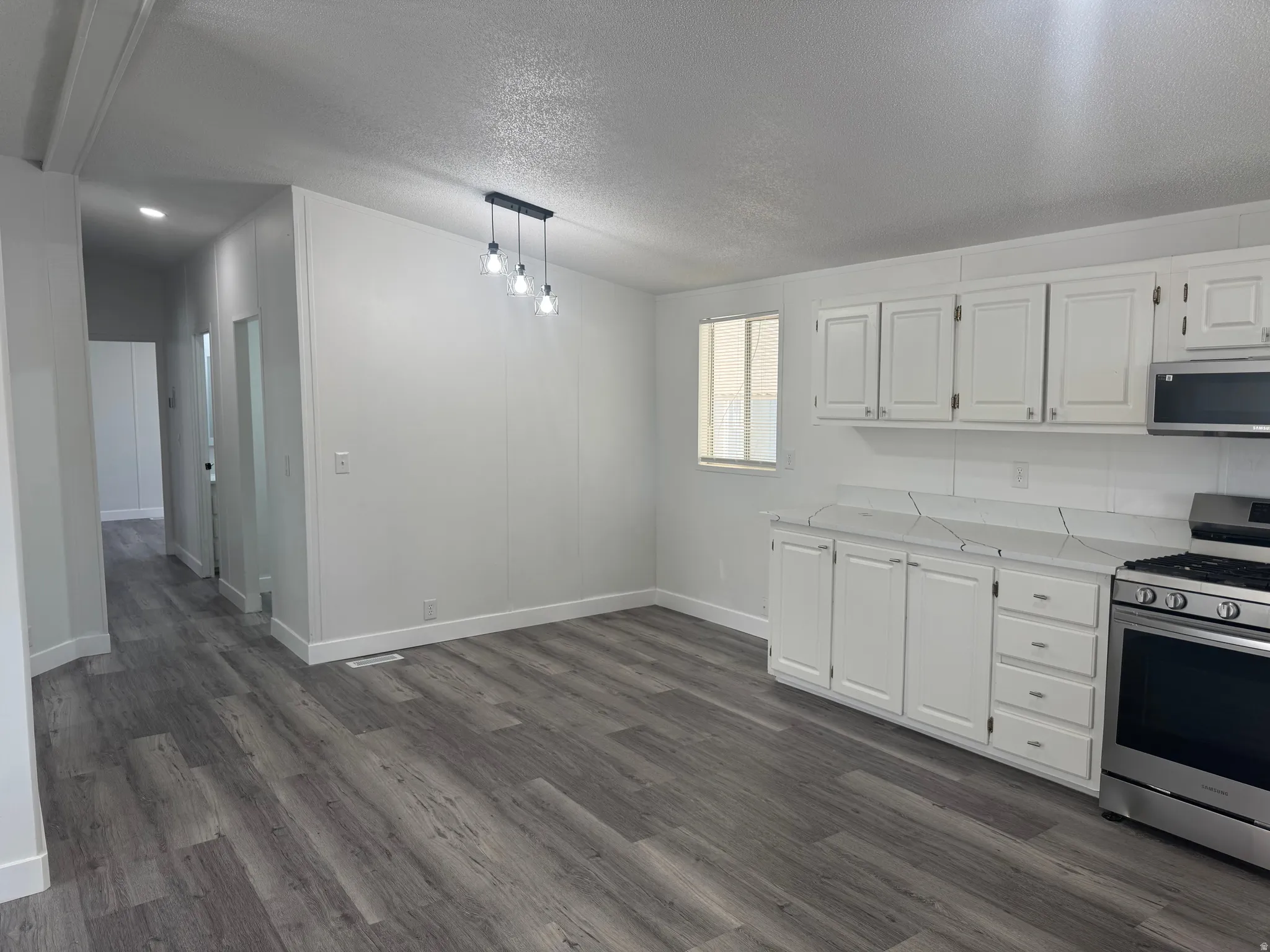 Open-concept living space featuring wood-finish flooring, white cabinetry, stainless steel range, stainless steel microwave, and recessed lighting