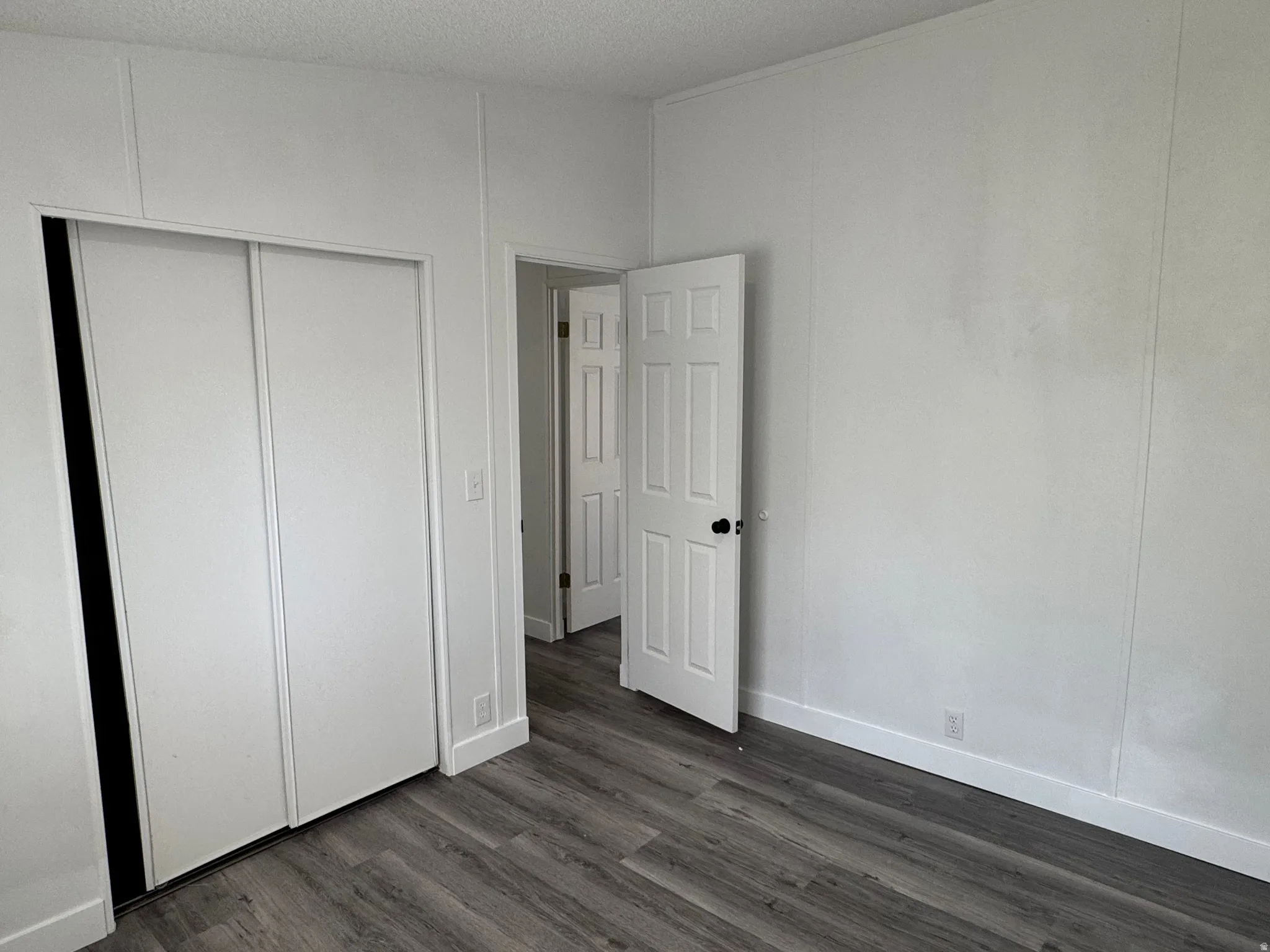 Interior room featuring wood-finish flooring, white paneled walls, and a white bi-fold closet door