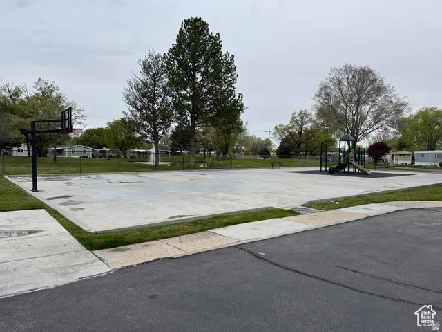 Outdoor recreational space featuring a concrete basketball court with a hoop, a children's playground with slides, surrounding green lawns, and mature trees