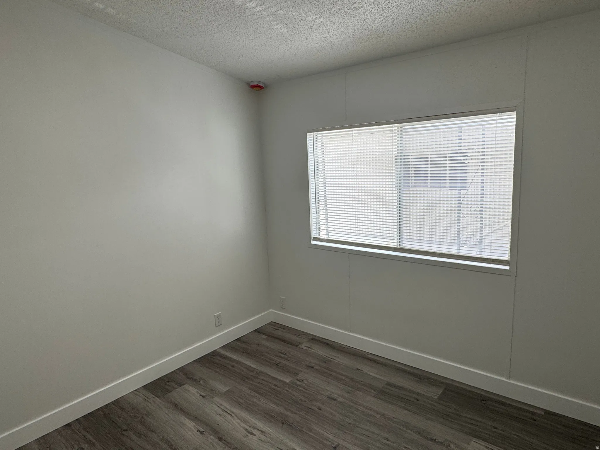 Room featuring a window with horizontal blinds, wood-finish flooring, and white baseboards
