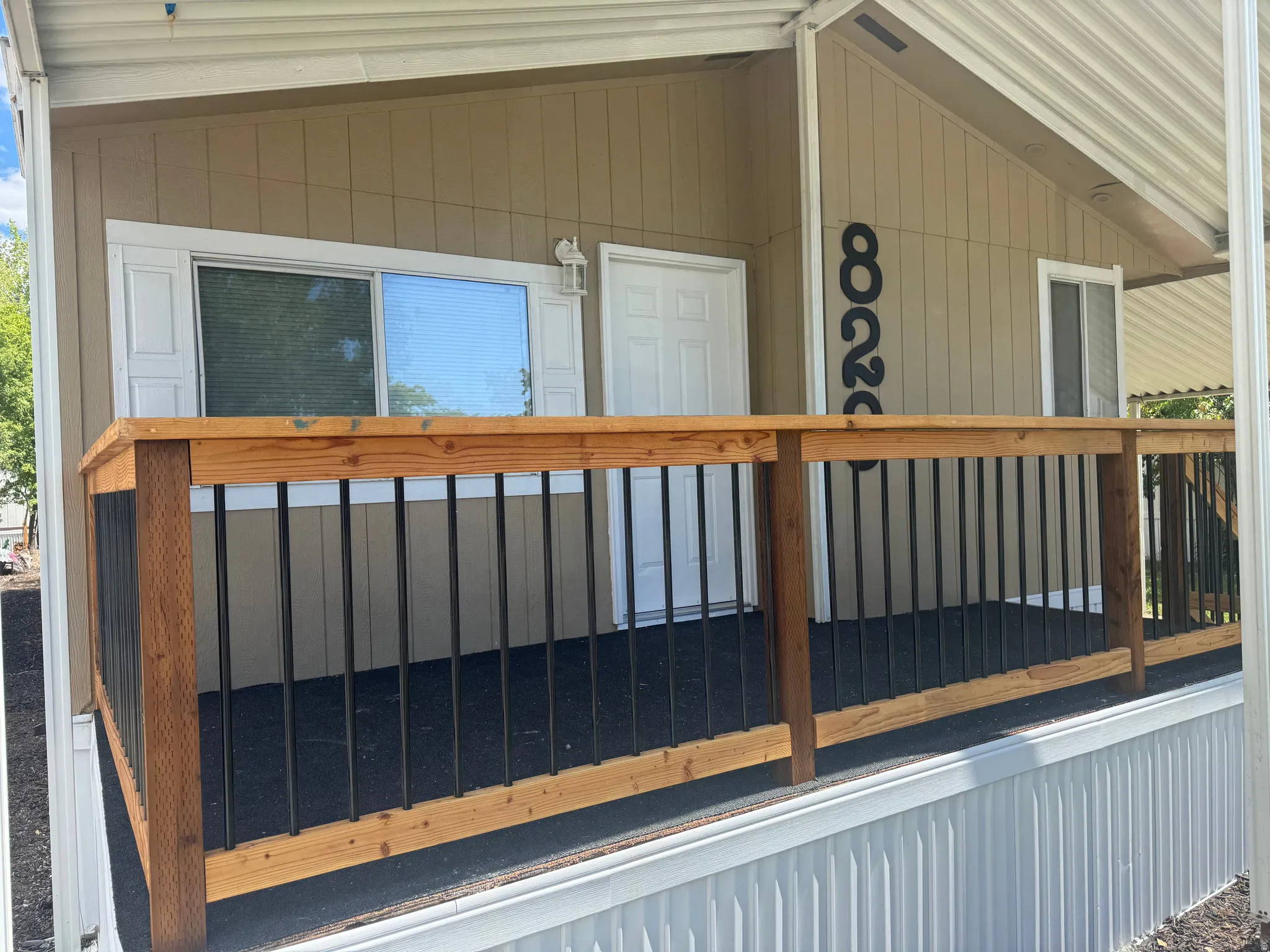 Covered entry porch featuring a wood railing with black balusters, a tan exterior siding, and white trim