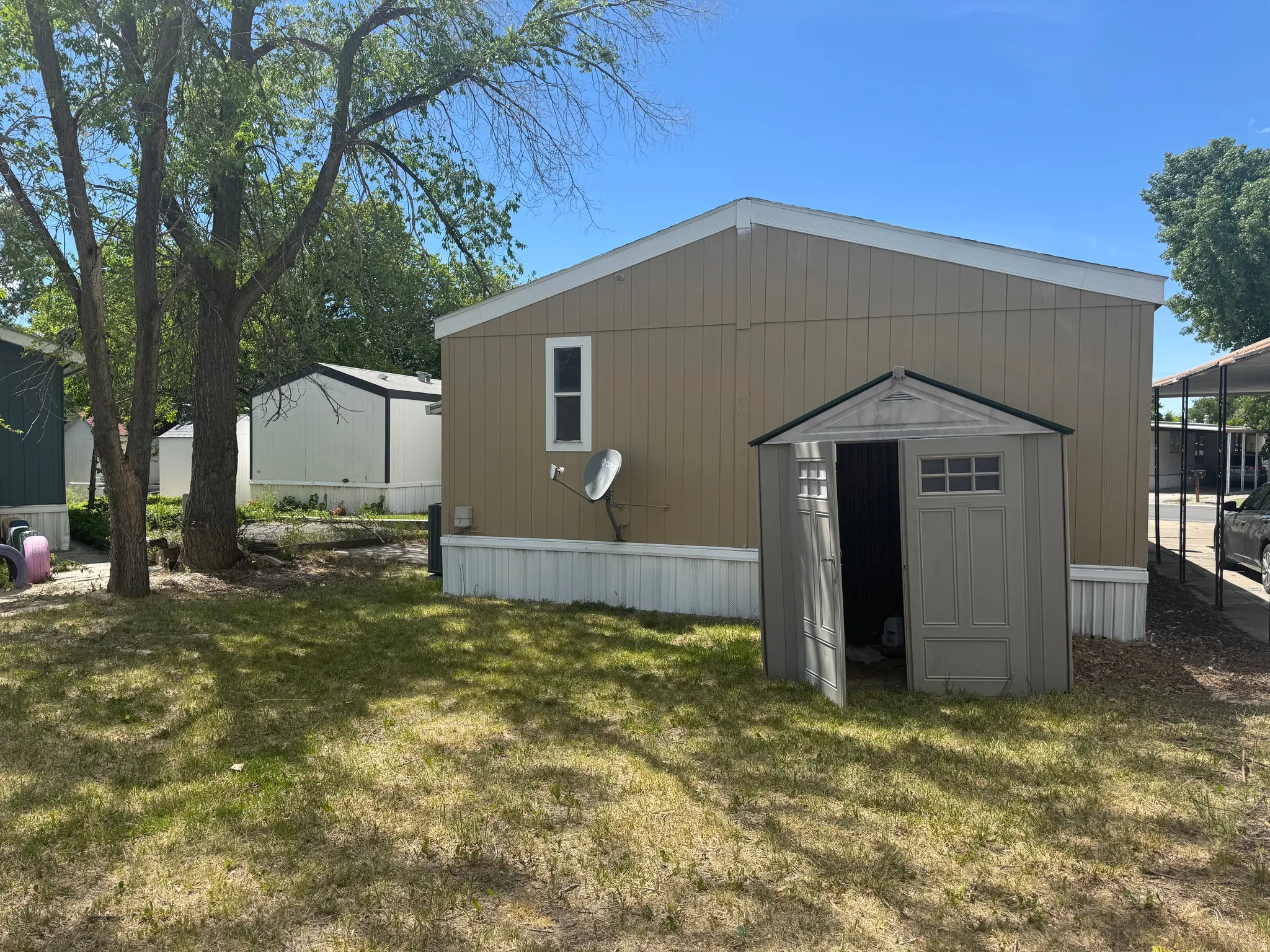 Tan exterior siding with white trim, featuring a side window and a separate storage shed