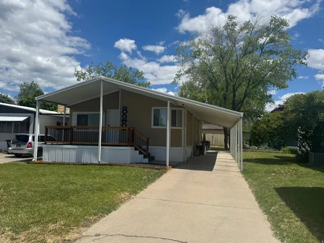 Tan siding residence featuring a covered front porch with wood-finish railing, an extended covered carport, a concrete driveway, and a grass lawn