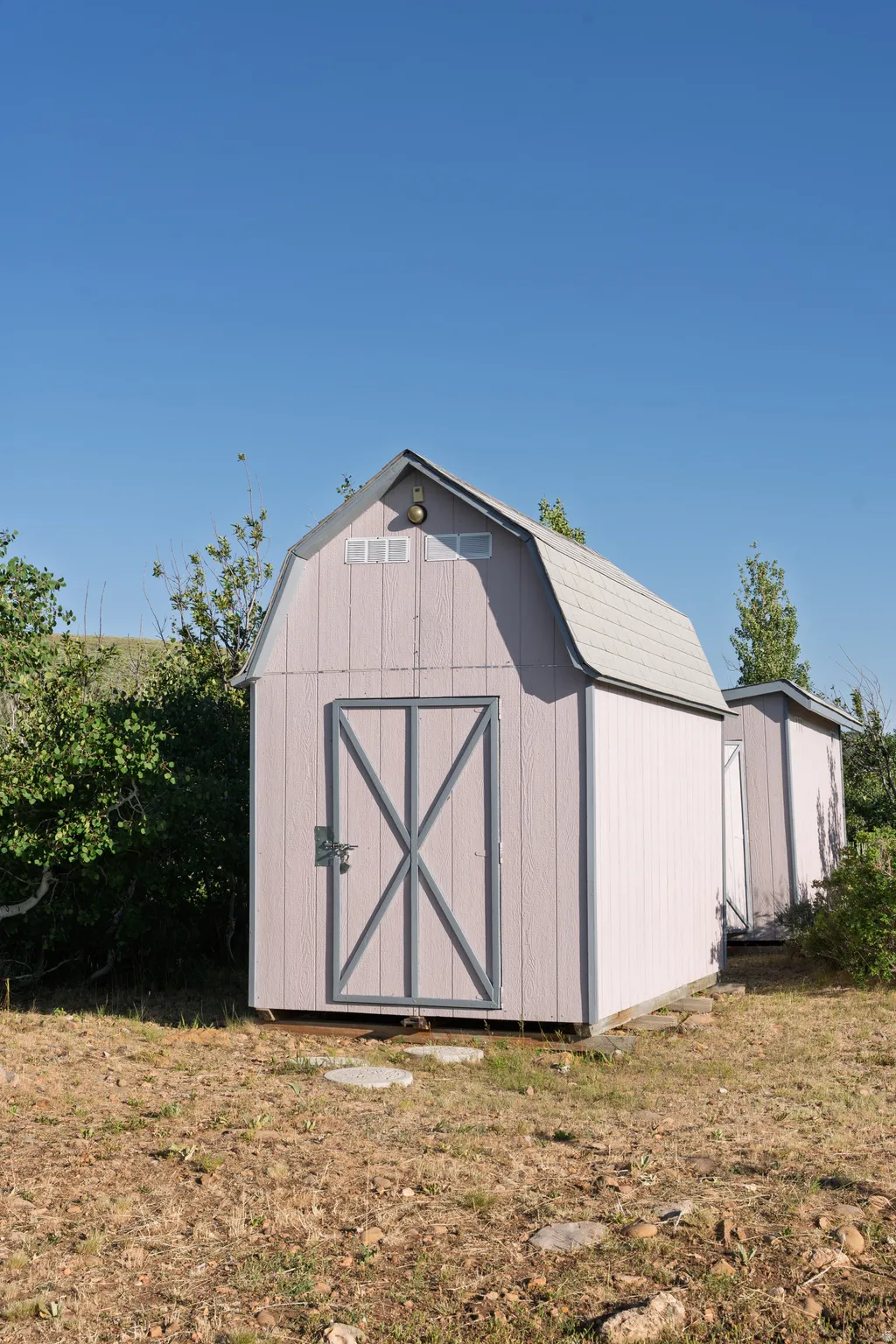 Barn-style storage shed with a gambrel roof and light-colored siding