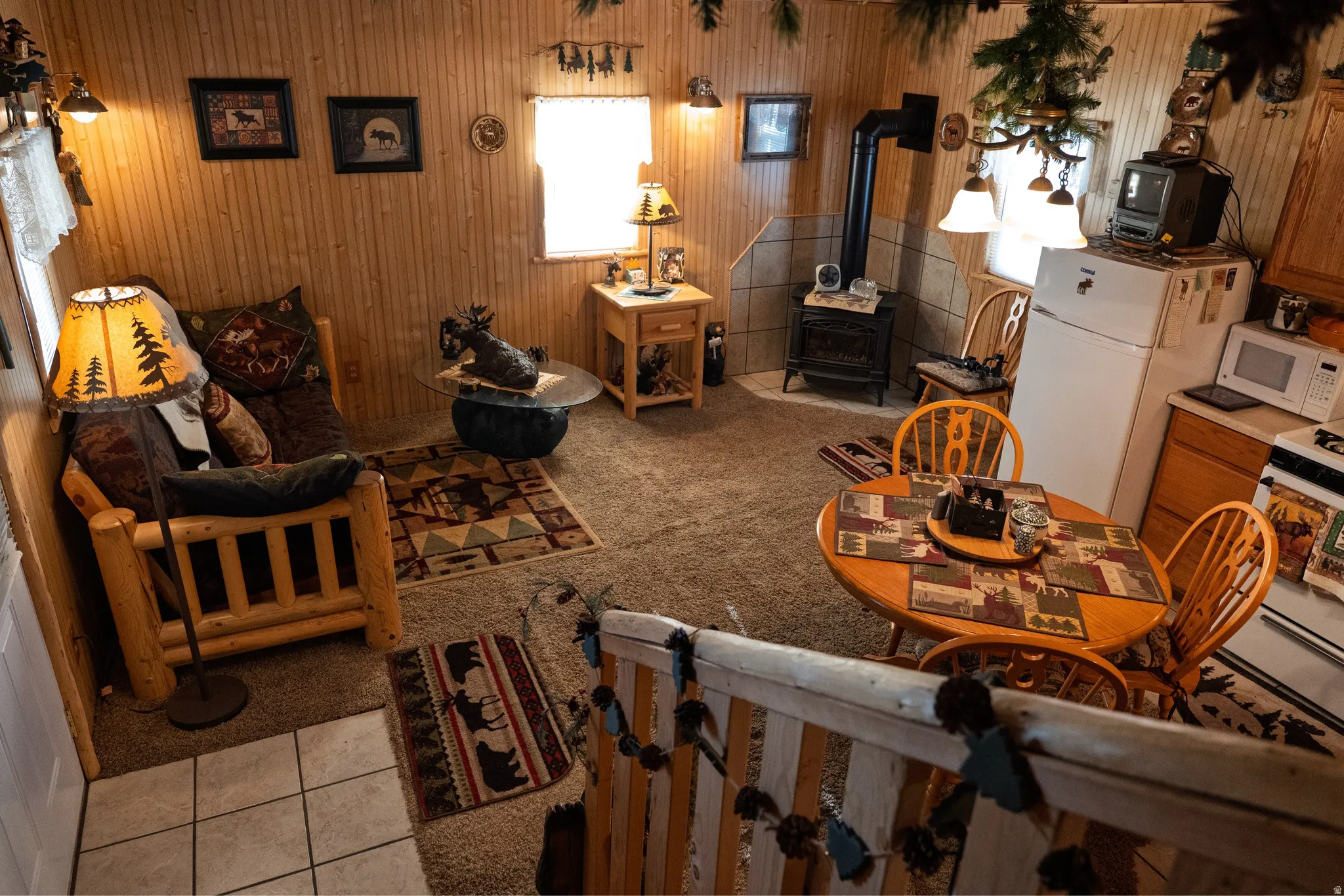 Interior featuring wood-paneled walls, carpet flooring, a compact kitchen with wood cabinetry, and a black wood-burning stove