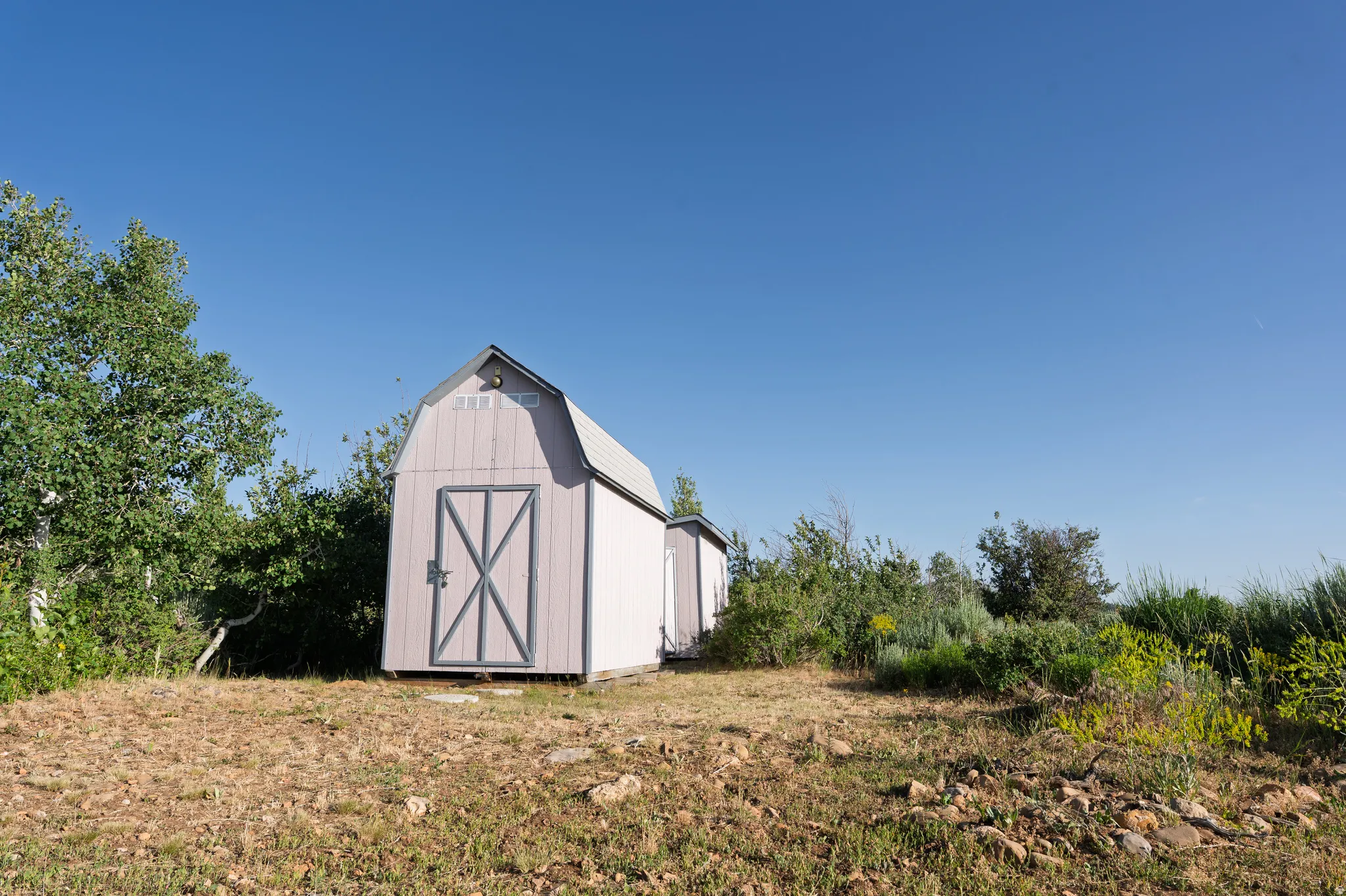 Gable roof outbuilding with double barn doors, light grey siding, and a metal roof