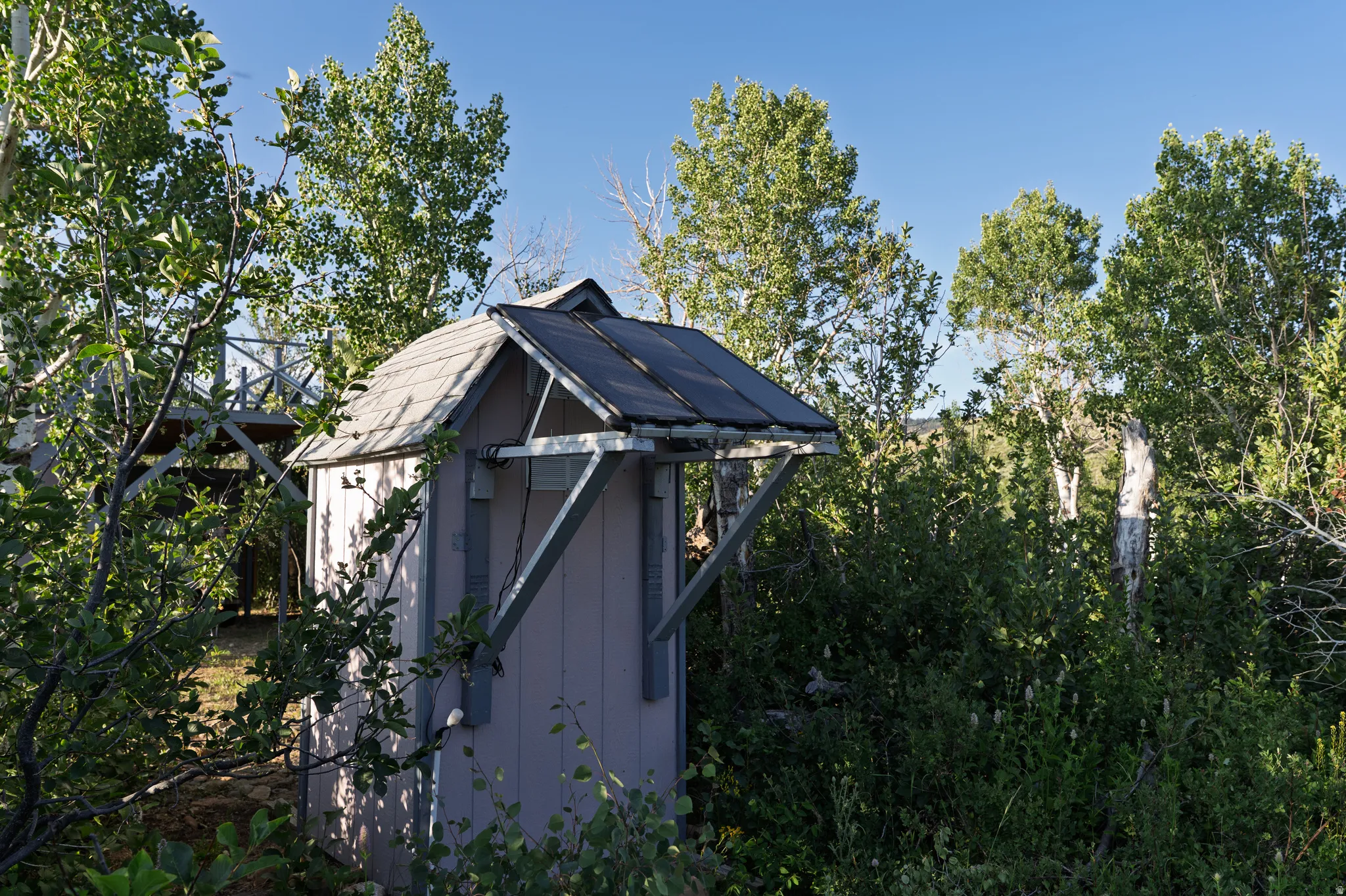 Compact outdoor structure featuring a shingled roof, light-colored siding, and an integrated solar panel
