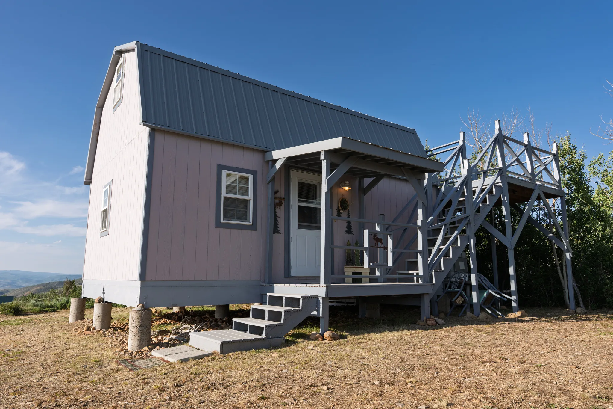Gabled structure featuring a metal roof, front porch with overhead coverage, exterior staircase, and an elevated platform