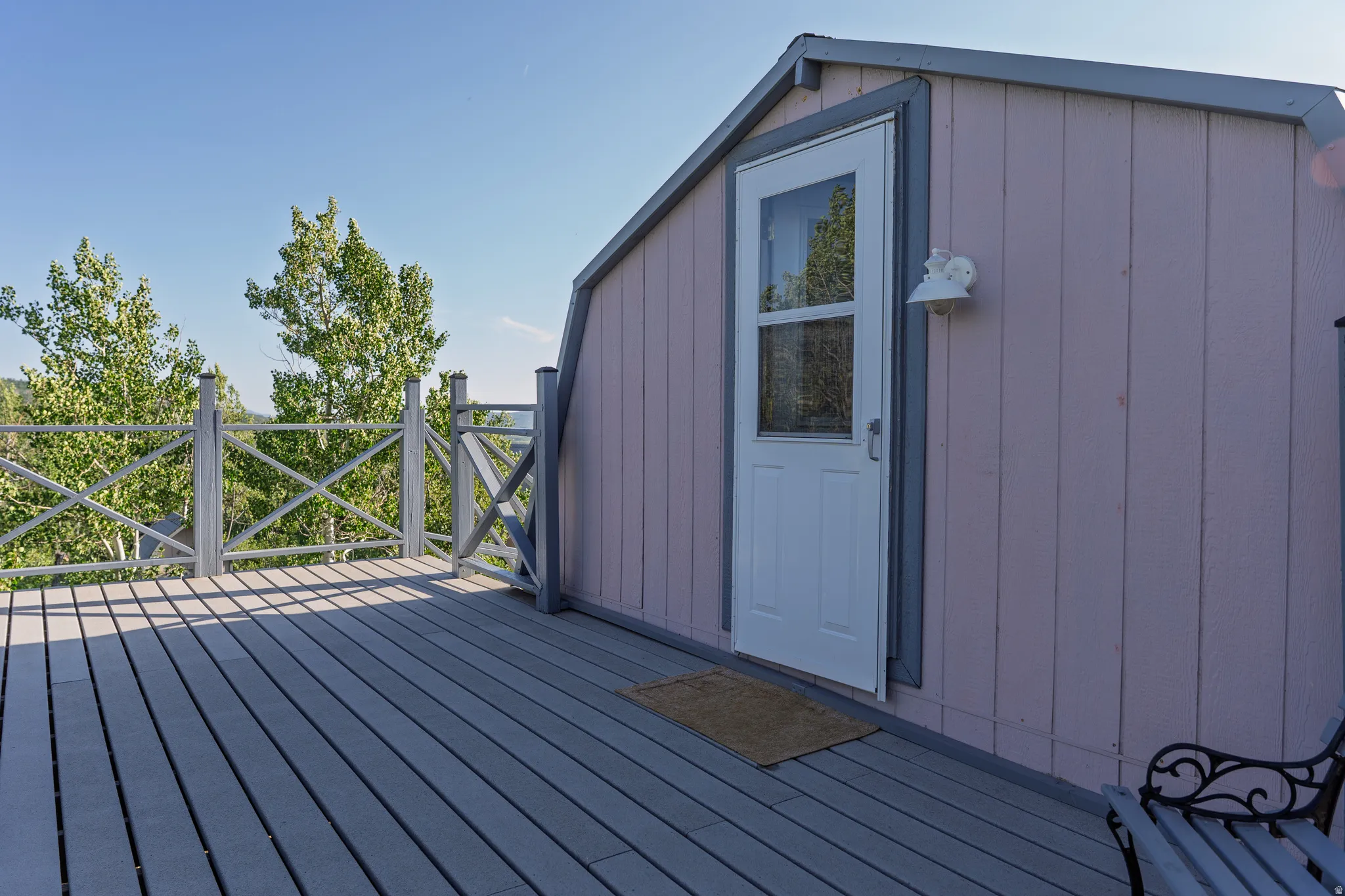 Elevated wood-finish deck with X-pattern railings, offering an exterior entry door with an overhead light fixture