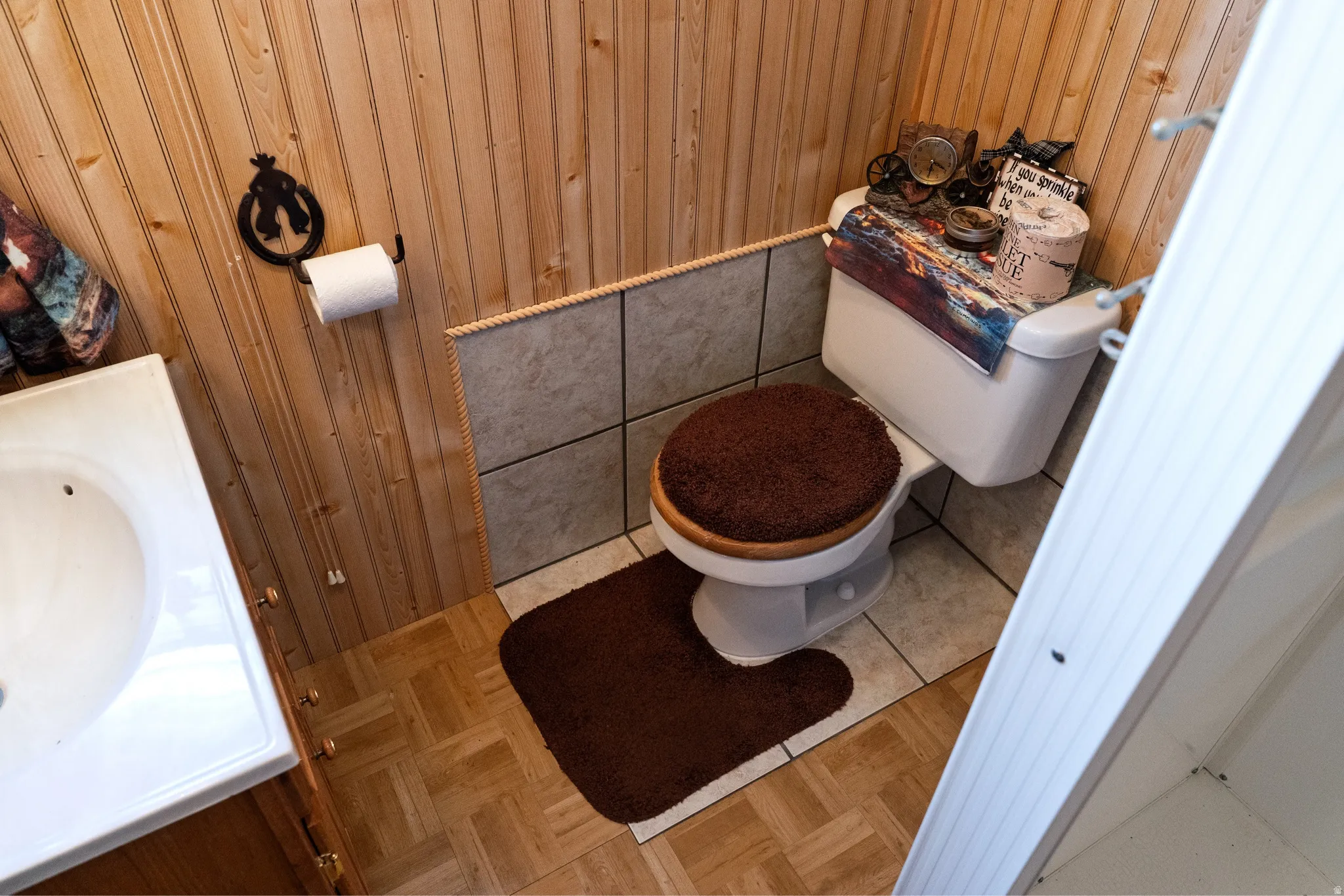 Bathroom featuring vertical wood paneling, a white porcelain toilet, a vanity with an integrated sink, floor tiling, and a tiled lower wall section
