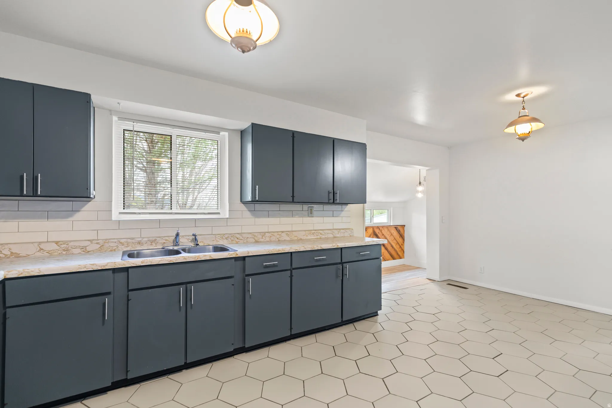Kitchen featuring gray cabinetry, a double basin stainless steel sink, a subway tile backsplash, and a window with blinds