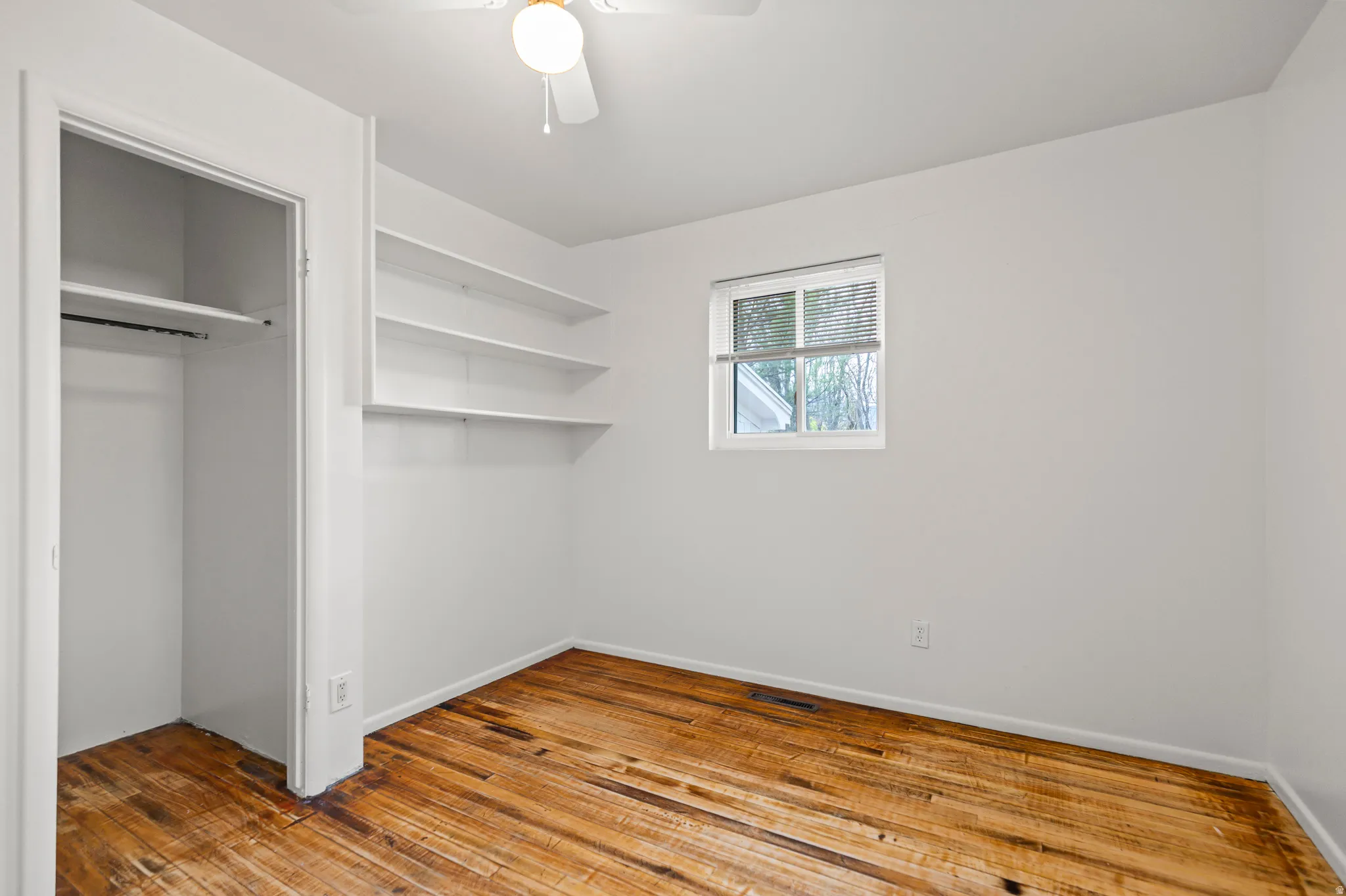 Room featuring wood-finish flooring, built-in shelving, and a window with horizontal blinds
