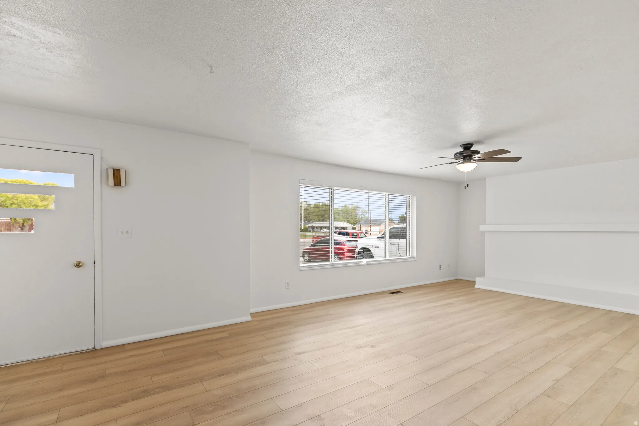 Spacious living area featuring light wood-finish flooring, white walls, and a contemporary ceiling fan with integrated lighting