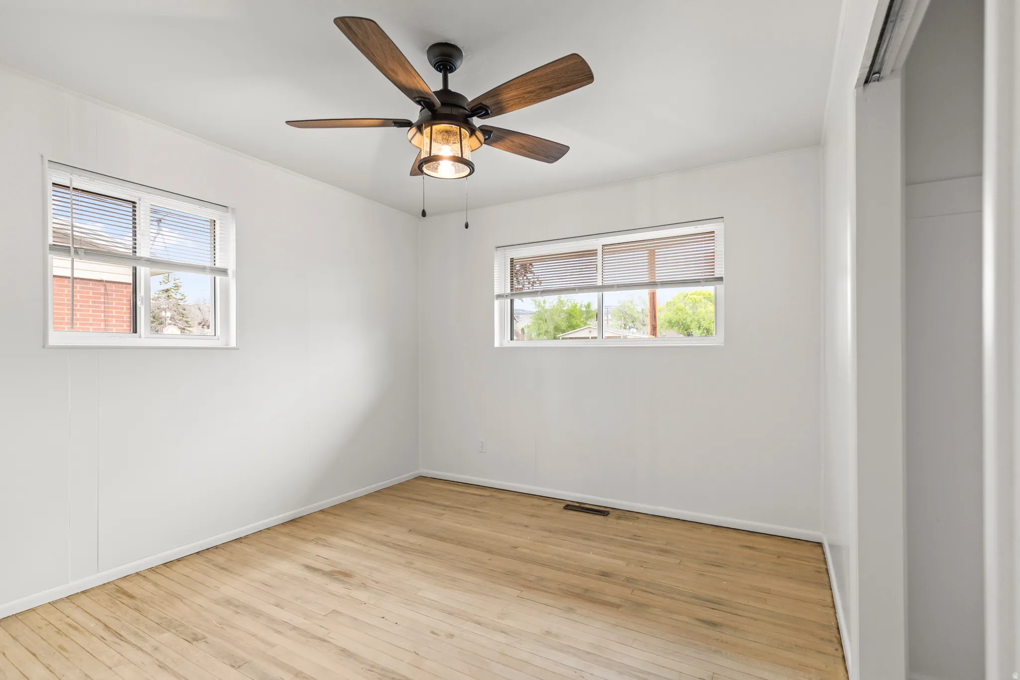 Wood-finish flooring and white walls define this room, featuring two windows with blinds