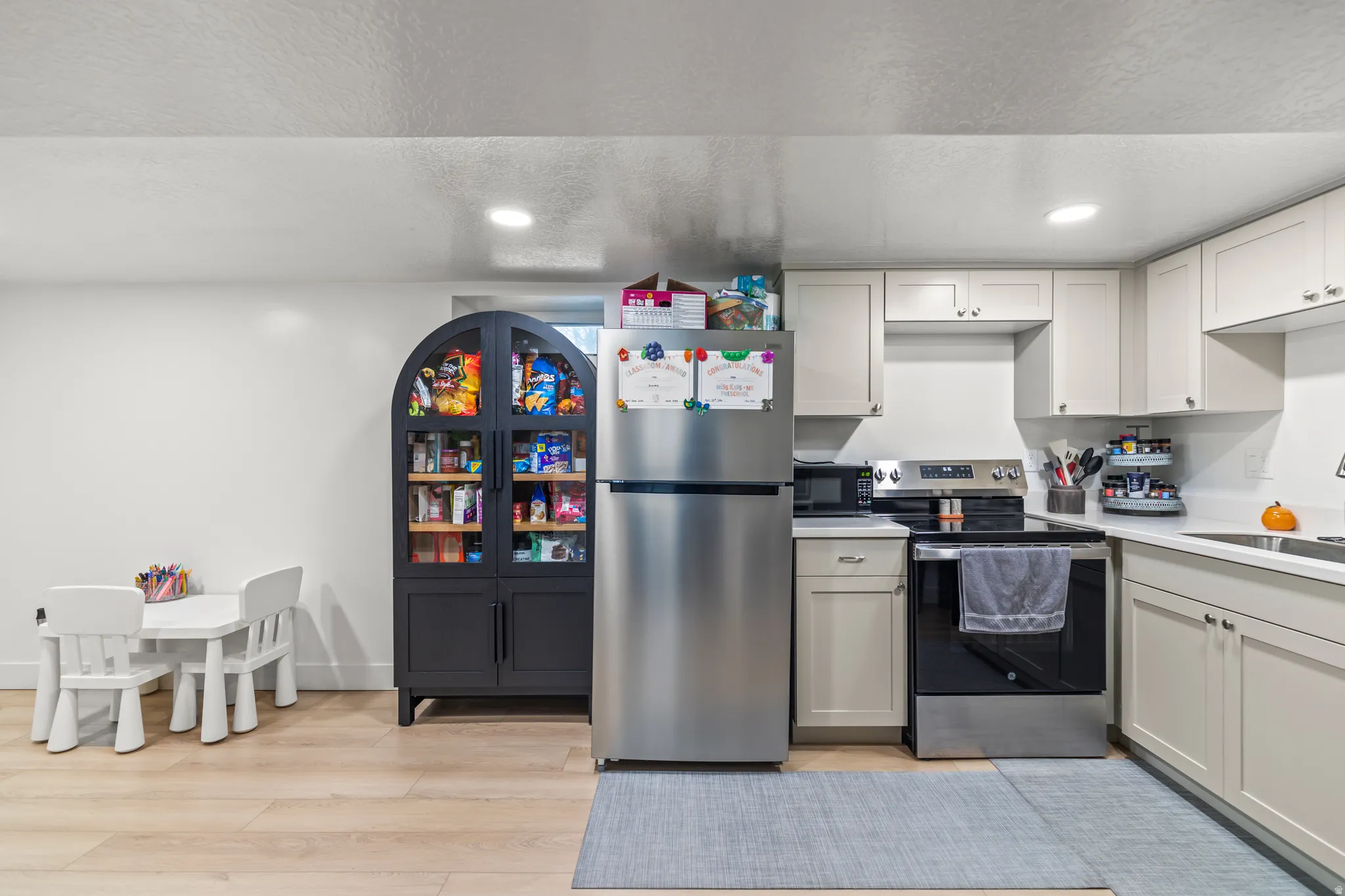 Compact kitchen featuring light-toned cabinetry, stainless steel appliances, and wood-finish flooring