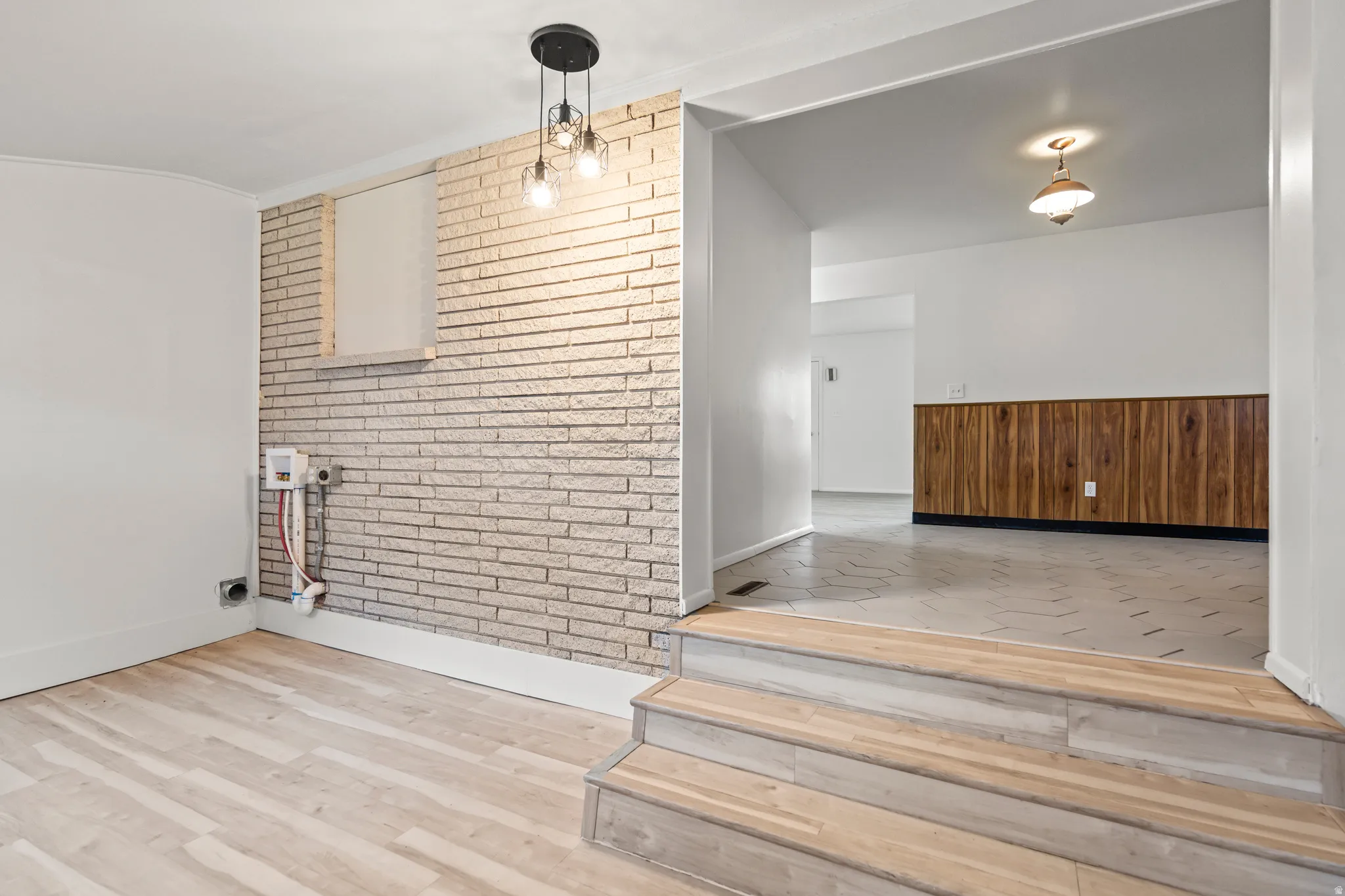 Split-level interior featuring light wood-finish flooring and a white painted brick accent wall