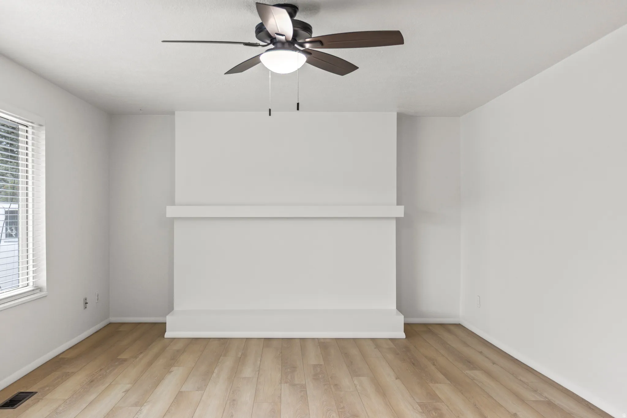 Living space featuring a prominent white fireplace, wood-finish flooring, a ceiling fan with integrated lighting, and a window with horizontal blinds