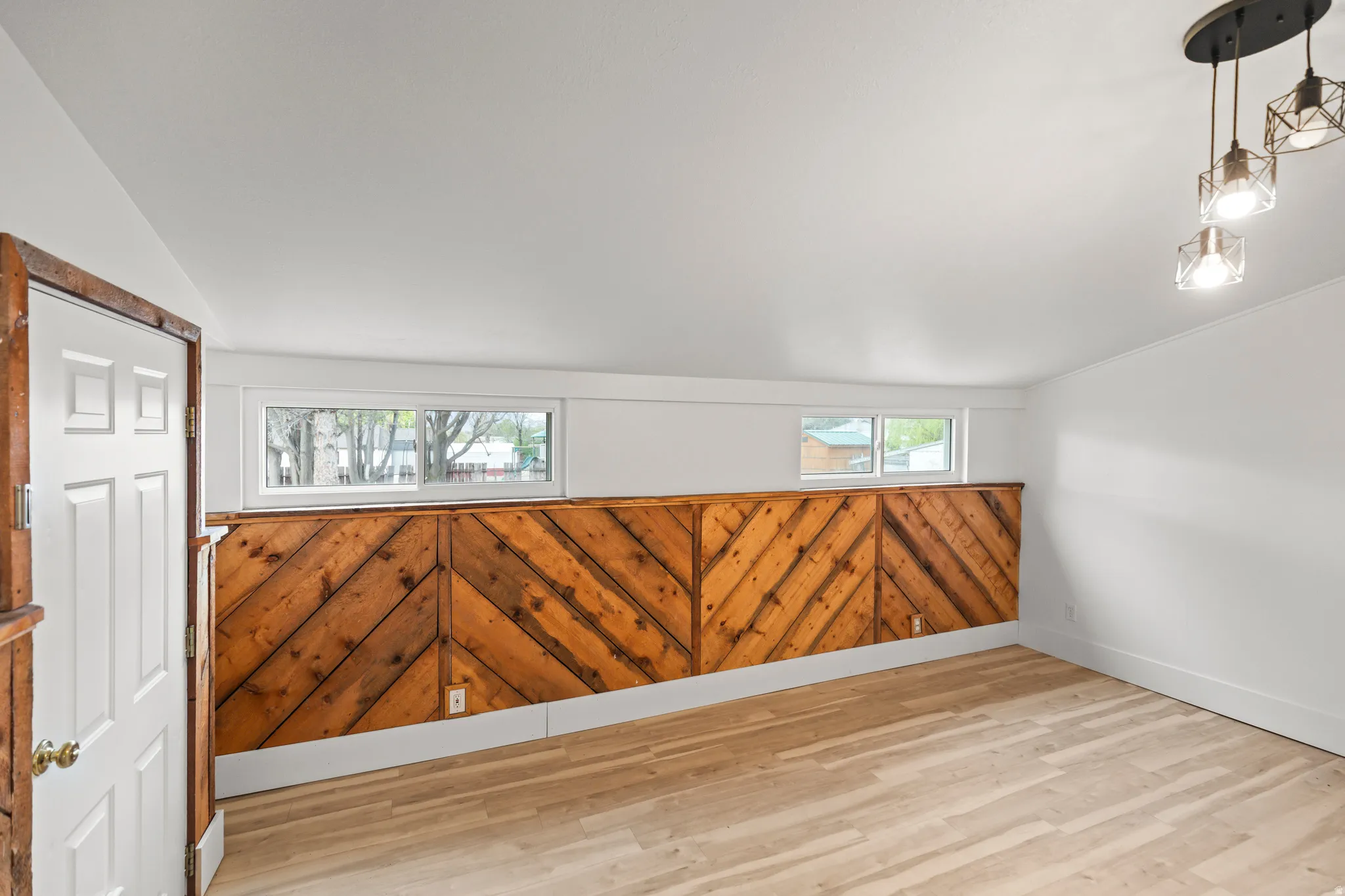 Interior space featuring wood-finish flooring, a decorative wood wall panel with a chevron pattern, and white painted walls
