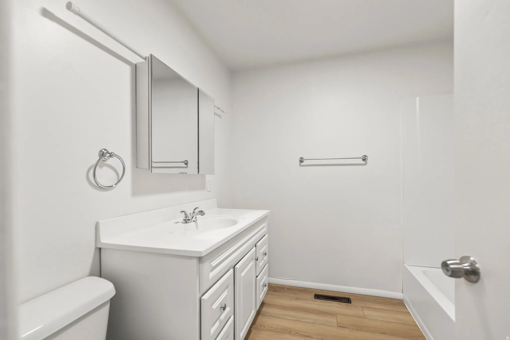 Bathroom featuring a white vanity with integrated sink, chrome faucet, medicine cabinet, and wood-finish flooring