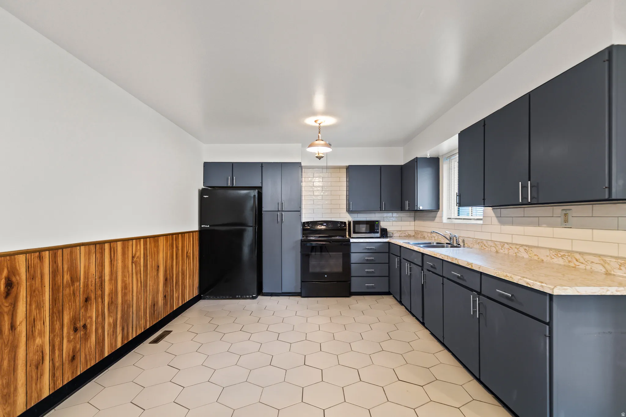 Kitchen featuring hexagonal floor tiling, dark cabinetry, light-toned countertops, a subway tile backsplash, and wood-paneled wainscoting