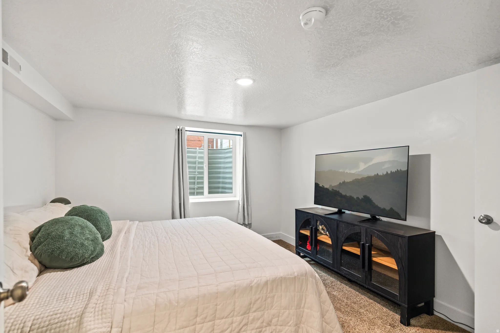 Comfortable bedroom featuring a window with privacy blinds, white walls, and a textured ceiling