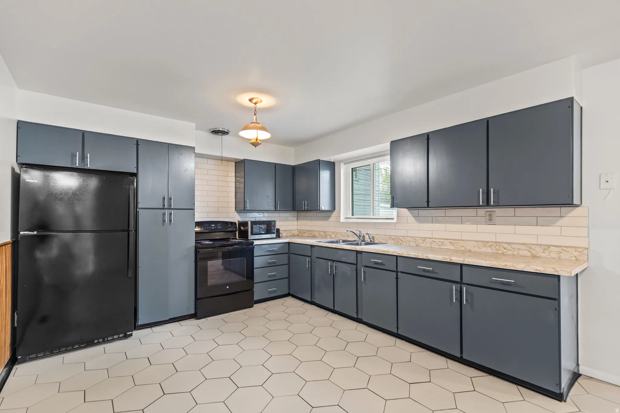 Kitchen featuring hexagonal floor tiles, gray cabinetry with silver hardware, a black appliance suite, light-colored countertops, and a subway tile backsplash