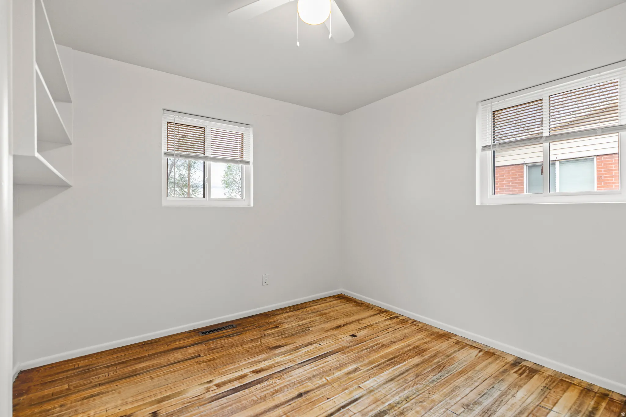 Room with two windows, painted white walls, wood-finish flooring, and a ceiling fan with integrated lighting
