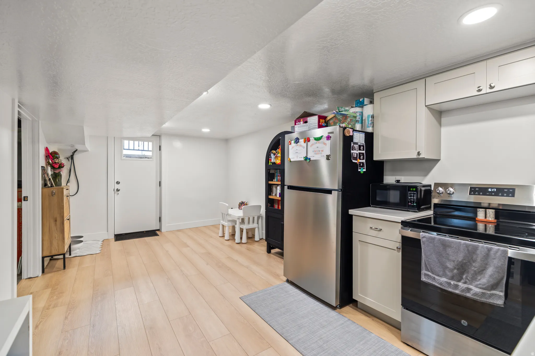 Kitchen area featuring light wood-finish flooring, white walls, recessed lighting, and a white entry door with a window