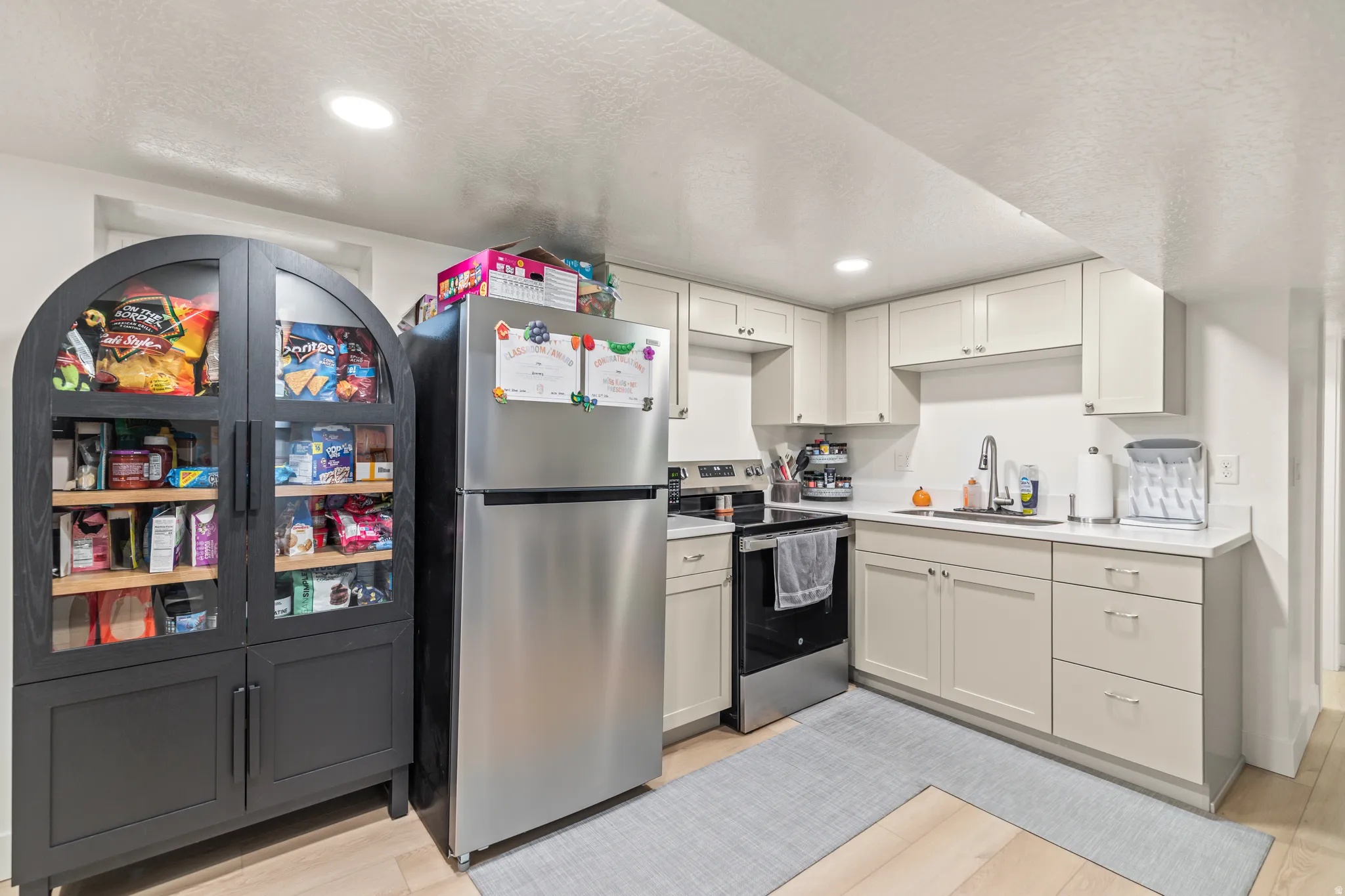 Compact kitchen featuring light-toned cabinetry, stainless steel appliances, and wood-finish flooring