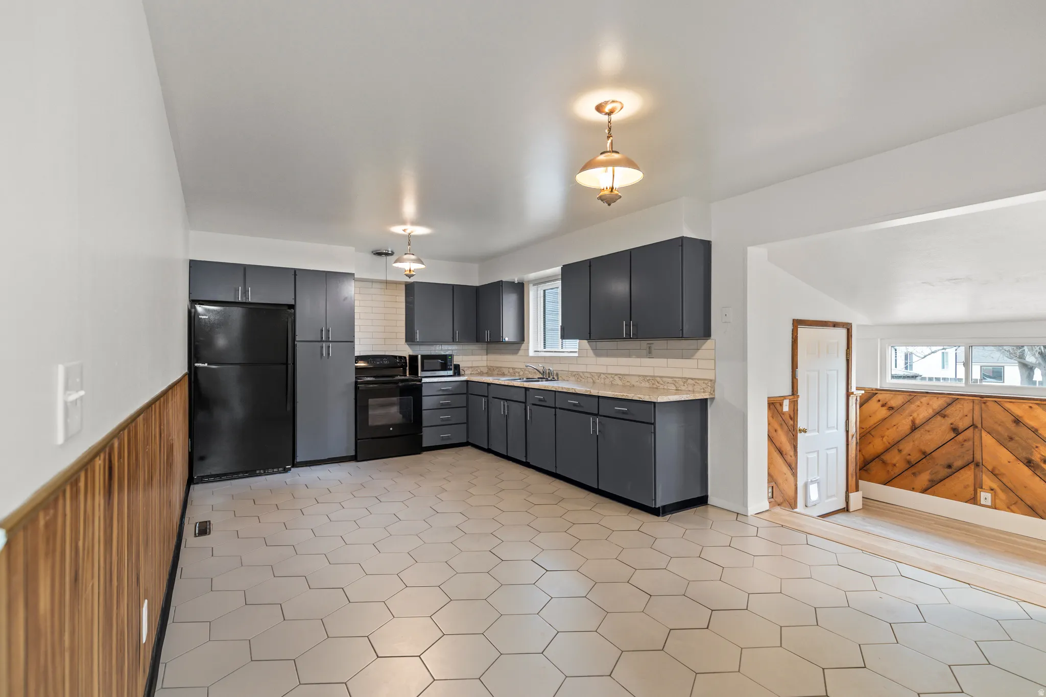 Kitchen featuring white hexagonal floor tiling, dark gray cabinetry, black appliances, and a white subway tile backsplash