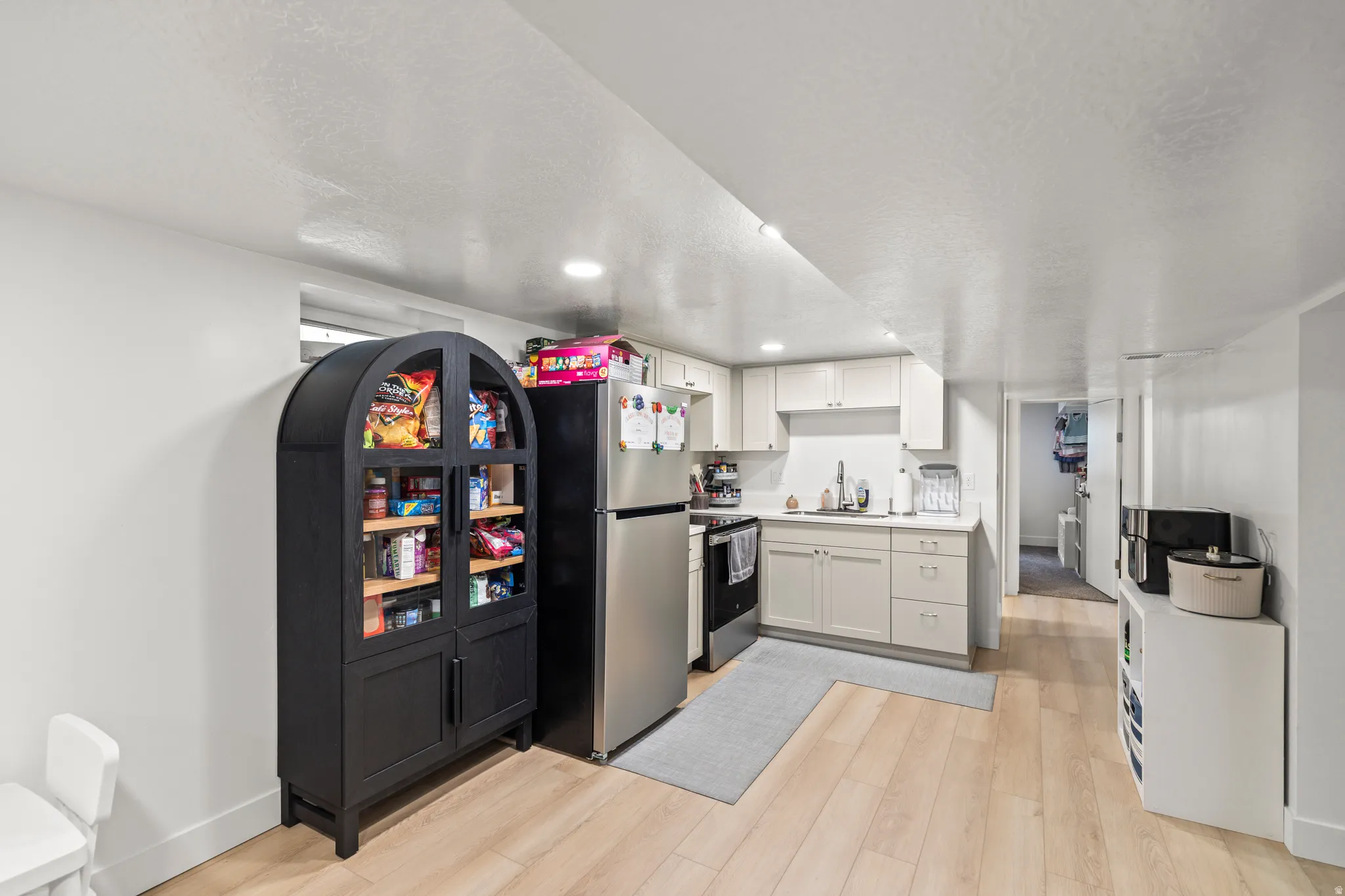 Compact kitchen area featuring light wood-finish flooring, recessed lighting, white cabinetry, and a stainless steel refrigerator