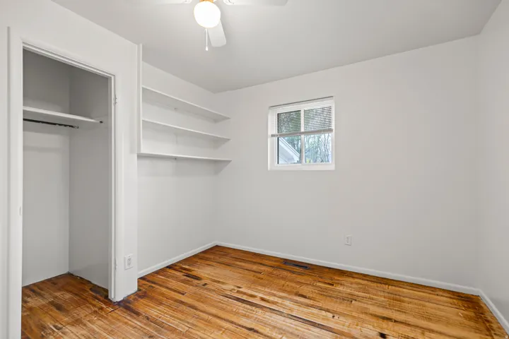 Room featuring wood-finish flooring, built-in shelving, and a window with horizontal blinds