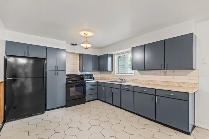 Kitchen featuring hexagonal floor tiles, gray cabinetry with silver hardware, a black appliance suite, light-colored countertops, and a subway tile backsplash