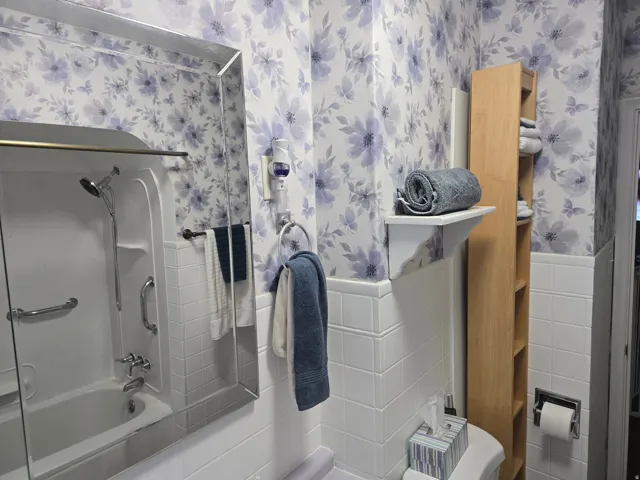 Bathroom featuring a white bathtub with a shower head, white tiled walls, and floral wallpaper