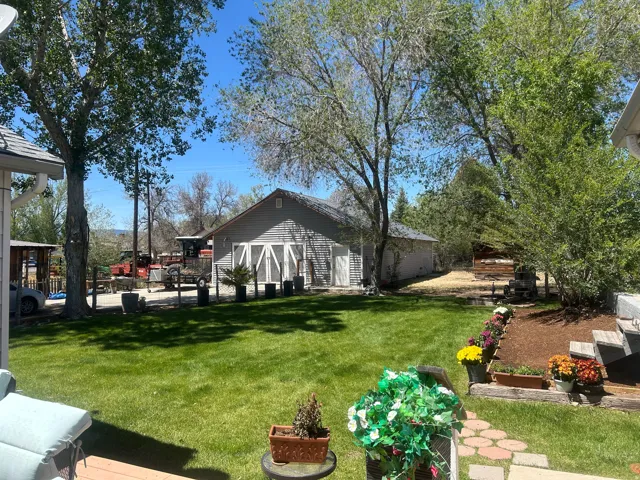 Expansive green lawn with mature trees and a detached outbuilding featuring a gray siding exterior and white barn-style doors