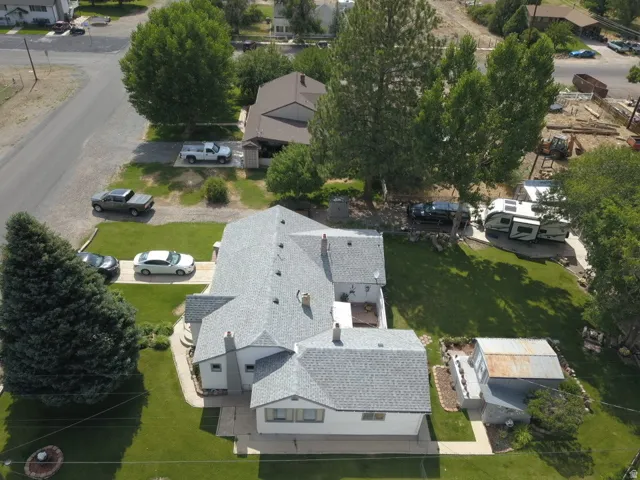 Expansive lot featuring a main residence with a light gray shingle roof, green lawn, established trees, and concrete driveways