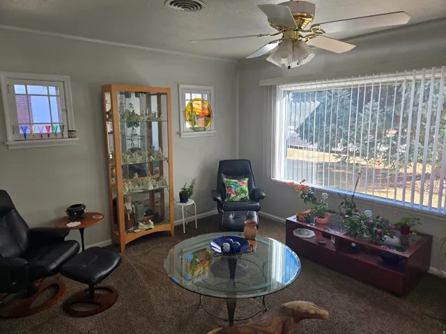 Living area featuring a ceiling fan with integrated lighting, a large window with vertical blinds, and two smaller accent windows