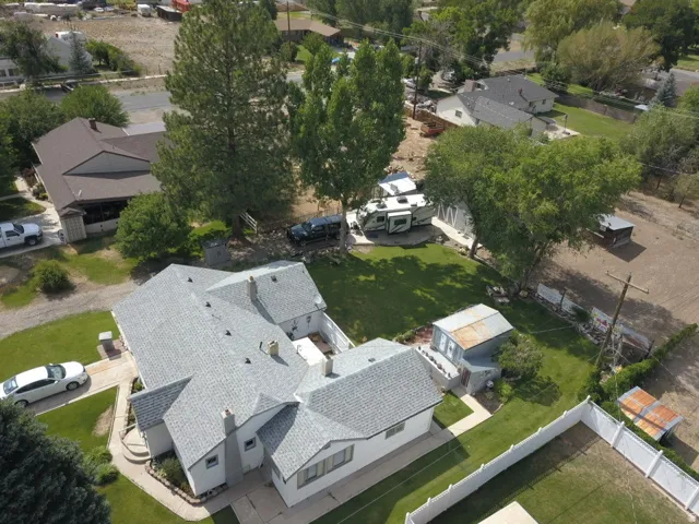 Property featuring a light gray shingle roof, white fencing, expansive lawn, and mature trees