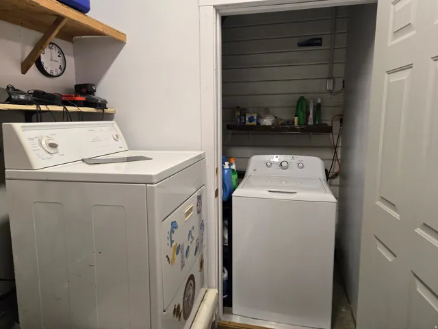 Dedicated laundry area featuring white appliances and wall-mounted shelving