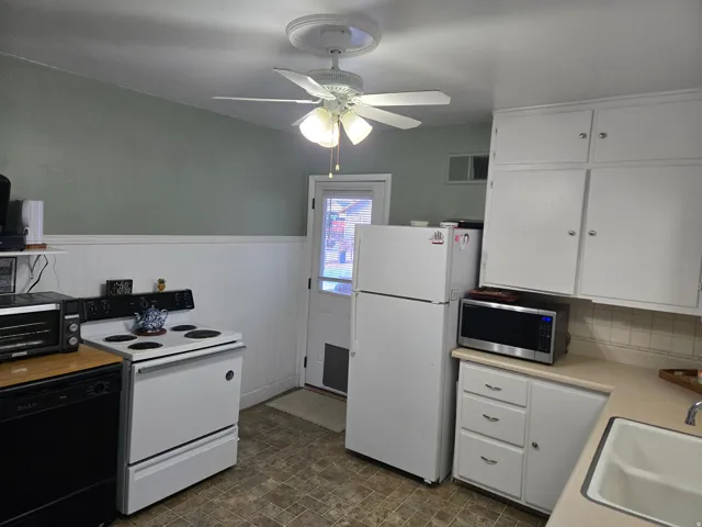 Kitchen featuring white cabinetry, white wainscoting, and a white ceiling fan with light fixture