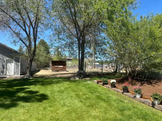 Expansive outdoor area featuring a manicured lawn, established shade trees, and a wooden storage shed