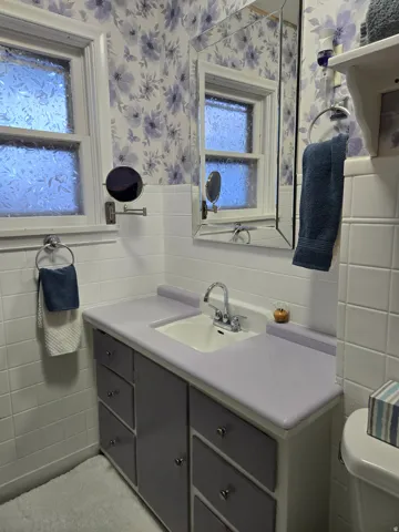 Bathroom vanity with a built-in sink, chrome fixtures, two casement windows with frosted glass, and white tile wainscoting